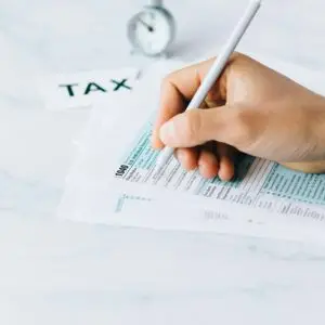 Hand completing tax forms with a pen, symbolizing financial deadline and time urgency.